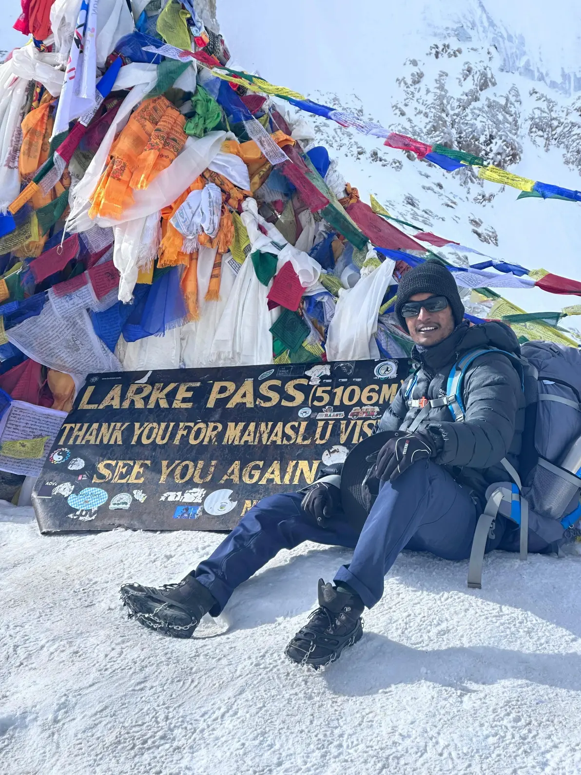 The Larke Pass sign at 5,106 m, prayer flags behind, on the Manaslu Circuit
